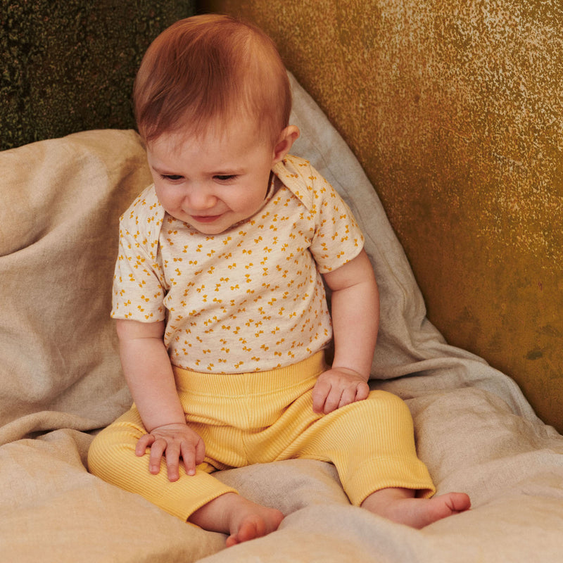 Babypige i printet body og leggings i gule nuancer fra Popirol. Babypigen sidder på hørdyne.