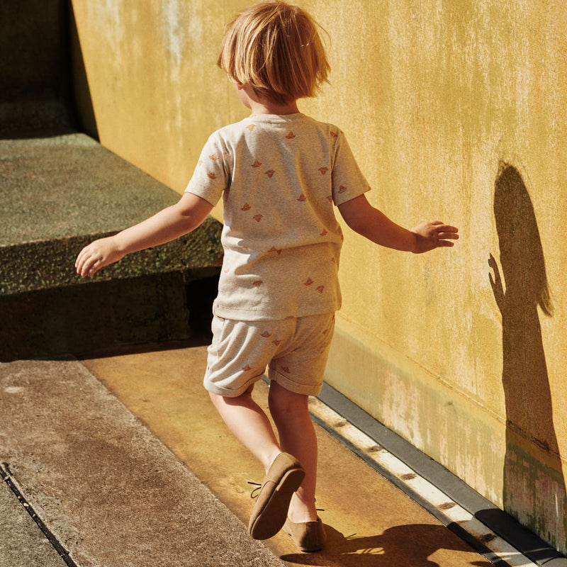Dreng i korte bukser og kortærmet T-shirt fra Popirol. Drengen går langs gul mur på en solrig dag. 